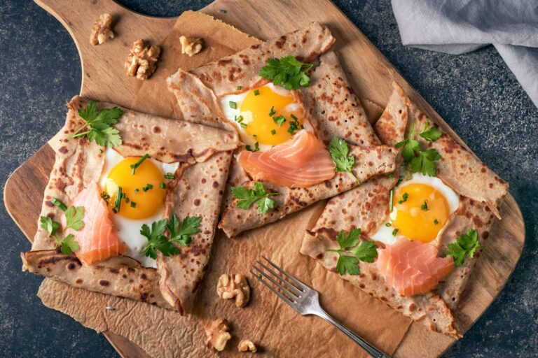 Photographie vue du dessus d'une galette au sarrasin qui contient un œuf, du saumon et quelques herbes aromatiques